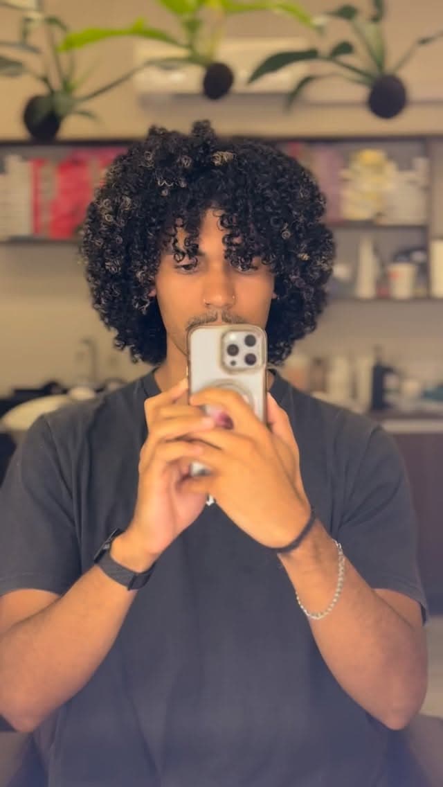 Rapaz de cachos definidos tirando foto no espelho do salão