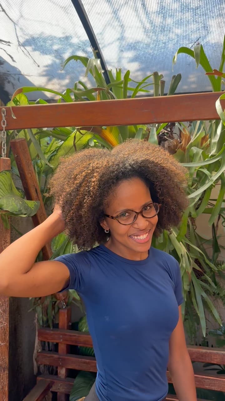 Cliente de cabelo crespo com a mão nos fios, no jardim de samambaias