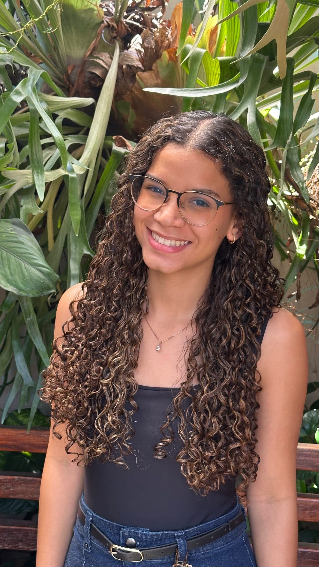 Cliente de cachos longos e óculos sorrindo no jardim do salão