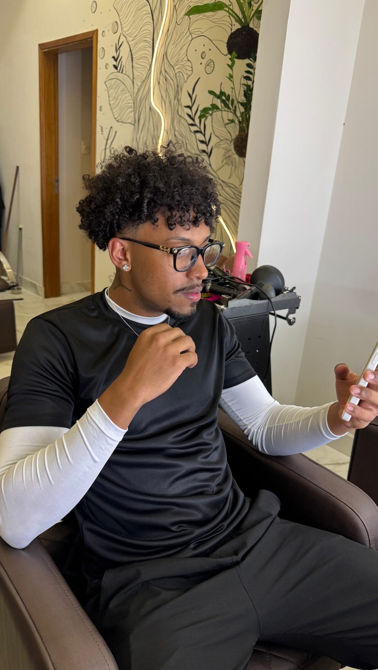 Rapaz de cabelo crespo e óculos sentado na cadeira do salão