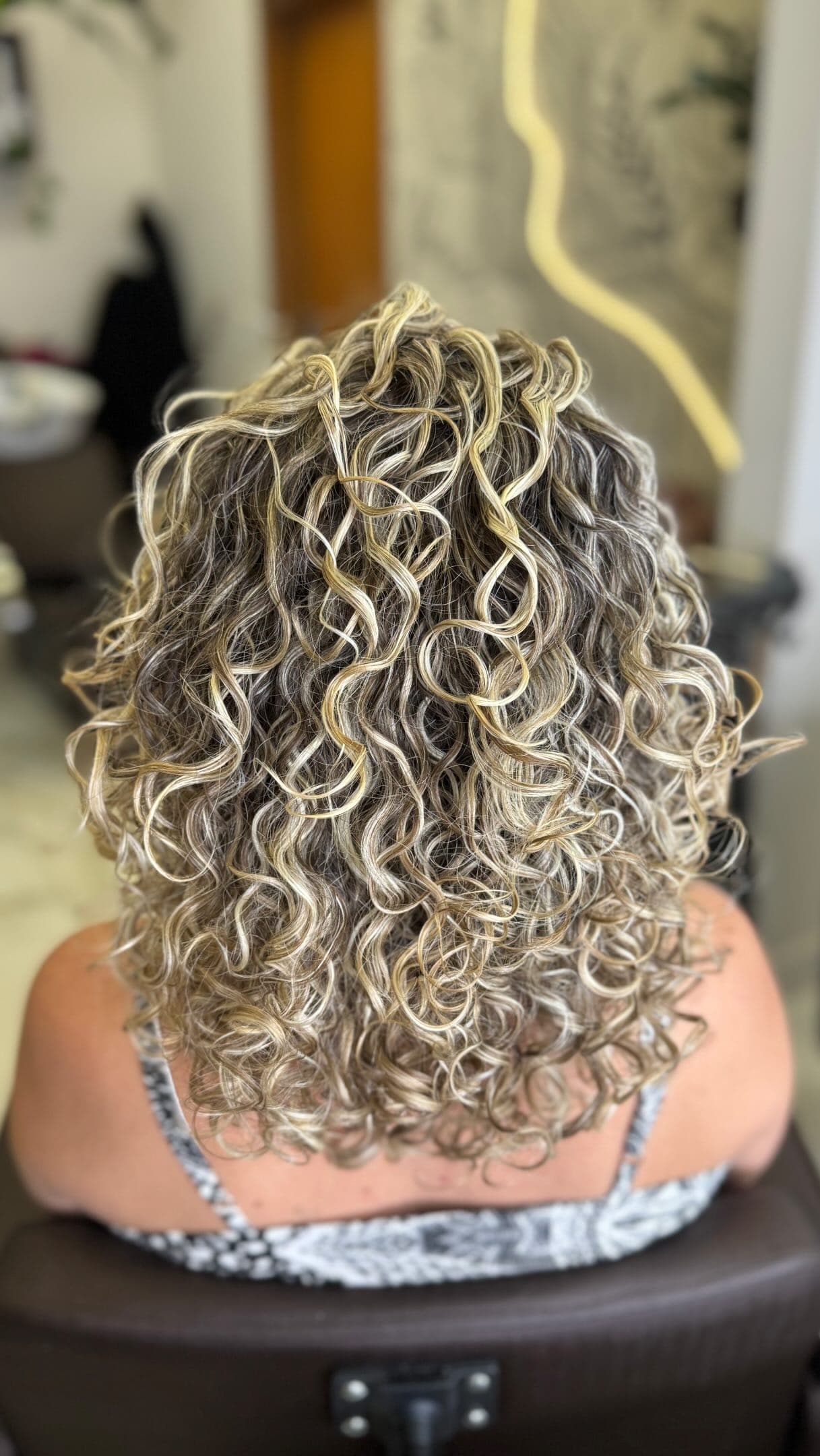 Cabelo cacheado com mechas claras, visto de costas na cadeira do salão